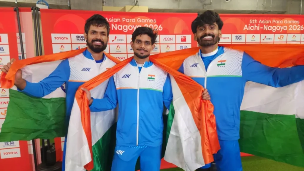 पुरुषों की T63 ऊंची कूद के तीनों पदक जीतने के बाद एशियाई पैरा खेल आइची-नागोया 2026 के बैकड्रॉप के सामने तिरंगा थामे भारतीय ऊंची कूद एथलीट शैलेश कुमार, वरुण भाटी और राहुल